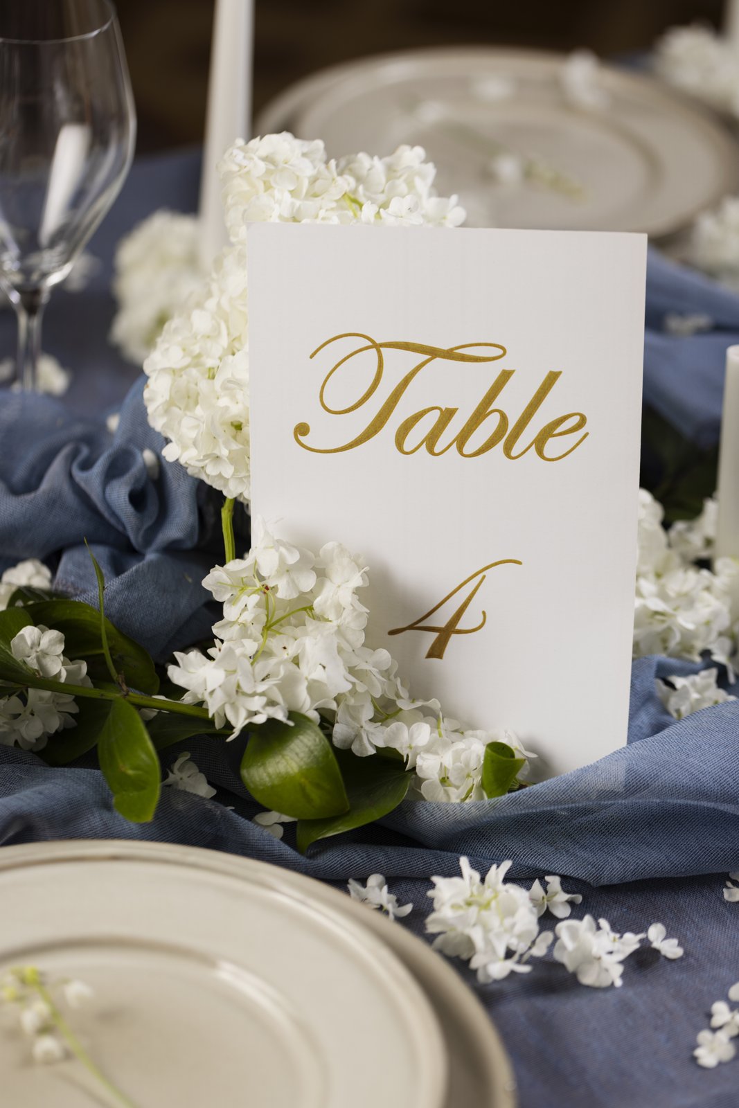 Gold foil wedding table number card with white hydrangeas on a blue table runner